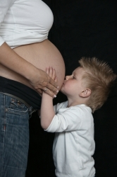 Kleiner Junge küsst Bauch der schwangeren Mutter