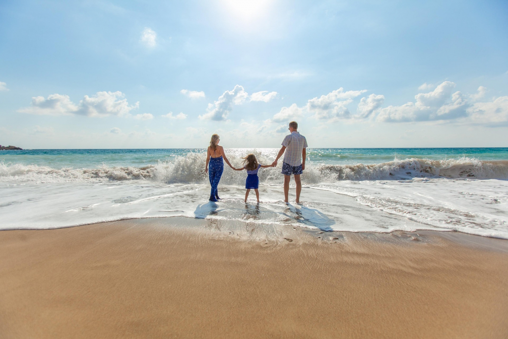 Eltern mit Tochter am Strand mit Blick auf Wellen - Rückenansicht